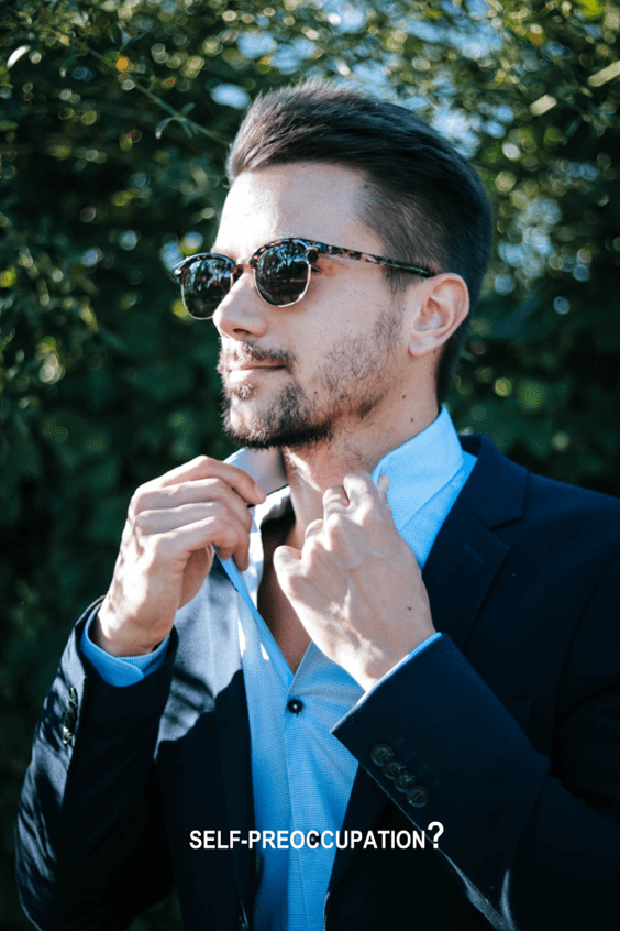 A man in sunglasses and suit adjusting his tie.