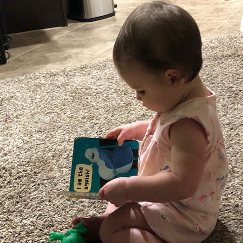 A baby sitting on the floor holding a book.